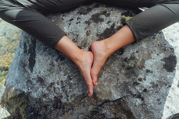 Človek sediaci na veľkom balvane, kedy sa chodidlami opiera o seba a nohy tak pripomínajú tvar srdca.