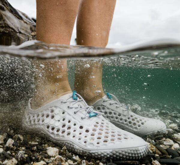 Pohľad na nohy vo vode v barefoot obuvi ULTRA, ktorá je vhodná aj do vody. Pod nohami sú kamienky.