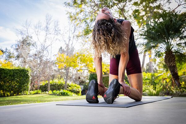 Žena je zohnutá v sede, ruky má za chrbtom a takmer sa opiera o päty.