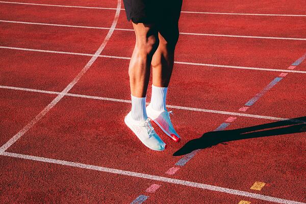 Muž v skoku na sy oranžovej bežeckej dráhe, obutý v najľahšej barefoot bežeckej obuvi VIVOBAREFOOT Primus Flow.