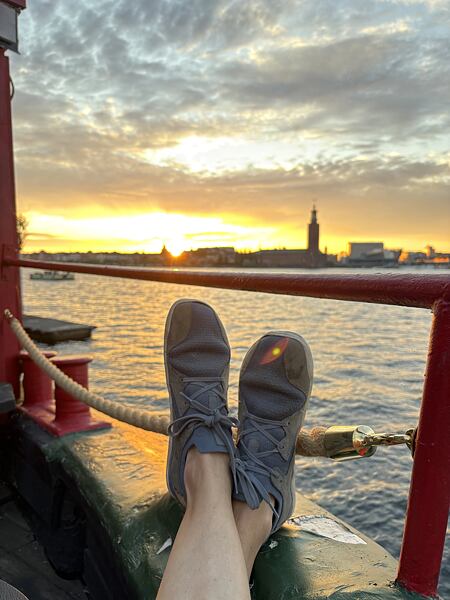 Autor článku sedí pri rieke pri západe slnka, v detailnom zábere má podopreté nohy v teniskách VIVOBAREFOOT, v pozadí vidno obrysy mestských pamiatok.